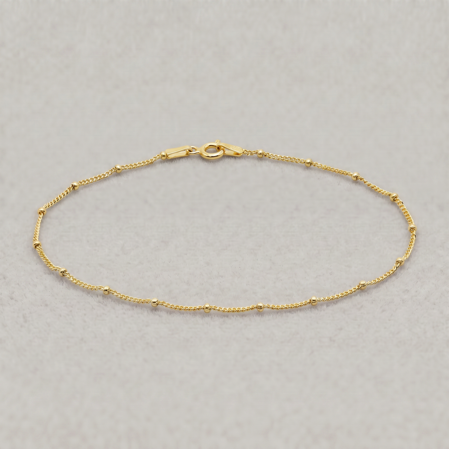 Gold plated sterling silver satellite bead curb chain bracelet, 1.2mm, on a plain background.
