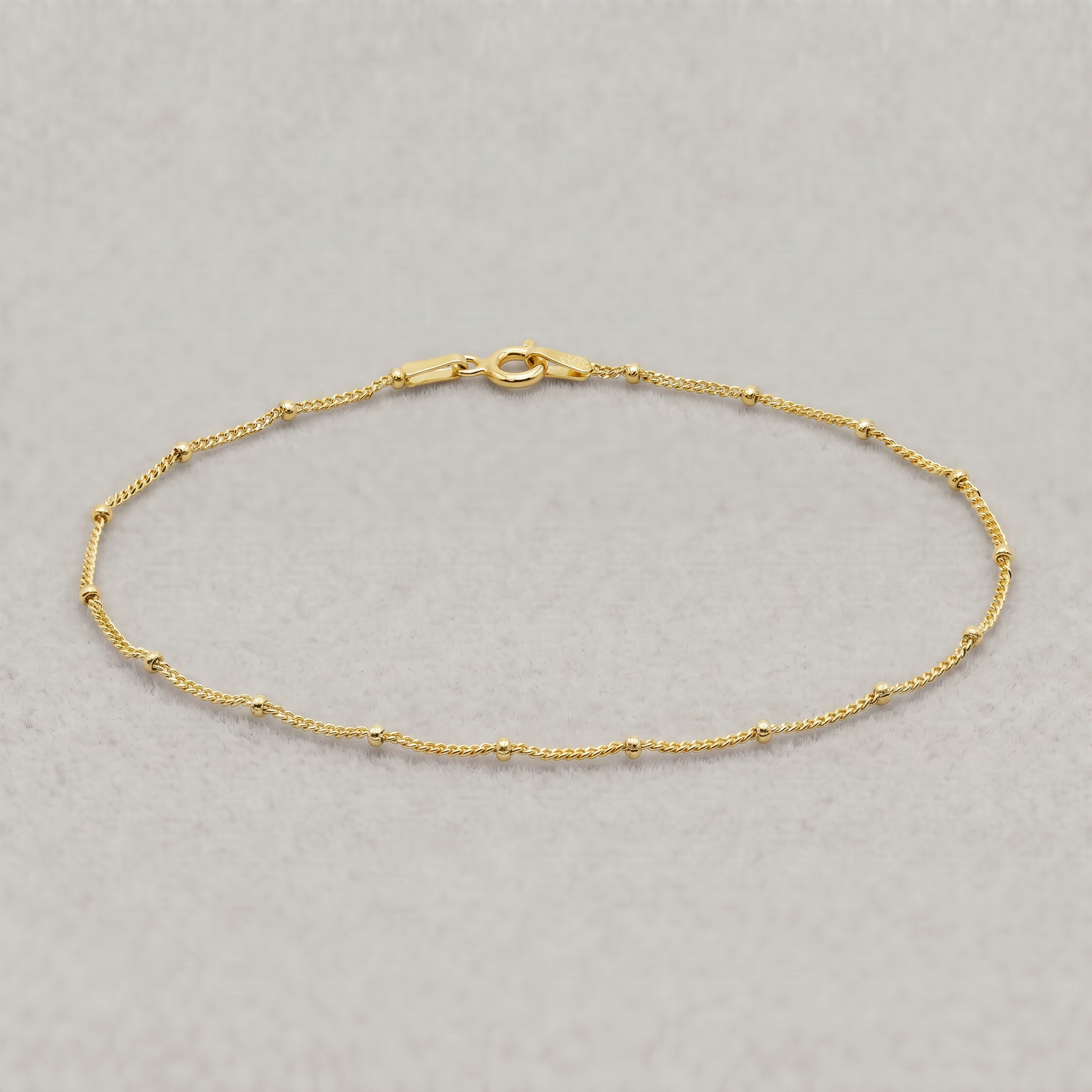 Gold plated sterling silver satellite bead curb chain bracelet, 1.2mm, on a plain background.